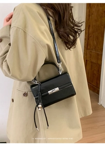 Side view of a black minimalist leather bag with silver buckle worn by a model in a trench coat