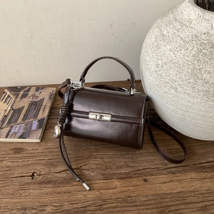 Detail of dark brown leather handbag with silver clasp and heart fringe on wooden table