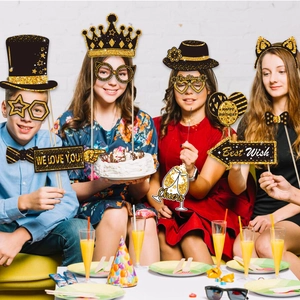 Teens using black and gold glittery photo booth props like crowns and funny glasses at a party