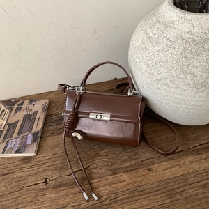 Detailed close-up of brown faux leather crossbody bag with silver twist lock and tassel