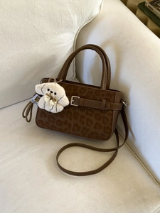 Sac à main léopard marron avec garniture en cuir et breloque chien sur canapé