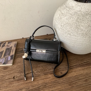 Detail of black glossy leather bag with silver buckle and heart pendant on wood table
