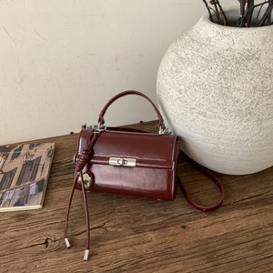 Detail of dark red glossy leather handbag with silver rotating lock on wooden table