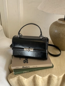 Minimalist black patent leather crossbody bag with silver hardware on vintage books