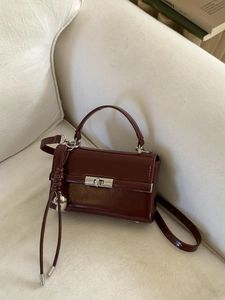 Elegant wine red square handbag with silver clasp and tassel on a white sofa backdrop