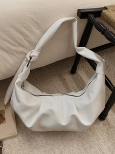 Ivory crescent hobo bag with knotted strap detail on a cozy cream woven blanket