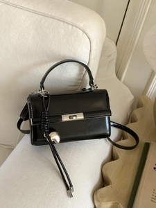 Minimalist black glossy leather crossbody square bag with silver metal lock on sofa