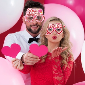 Couple wearing 'Be My Valentine' heart party glasses with red and pink balloon backdrop