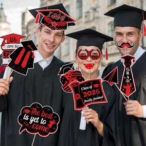 Three students in robes holding Class of 2026 graduation photo props on campus