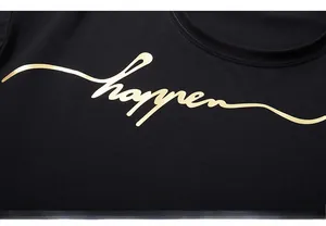 Dettaglio macro della stampa dorata happen su t-shirt nera in cotone con finitura lucida