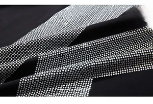 Détail macro de strass argentés et impression de lettres oranges sur tissu noir tricoté
