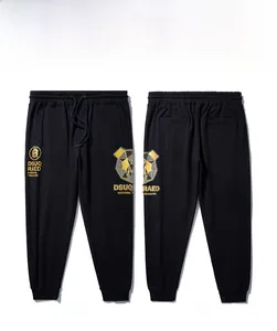 Détail d'un pantalon de jogging noir avec tête d'ours dorée et lettres DSUQ RAED