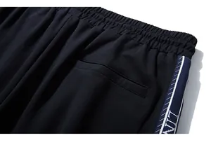 Detail of elastic waistband and side blue stripe webbing with lettering on black joggers