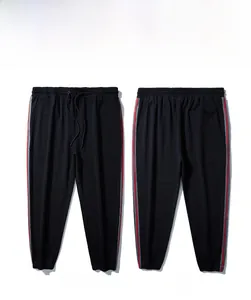 Detail of men's jogger pants showing red stripes and drawstring waist on black fabric
