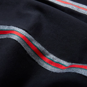 Black sporty track pants featuring distinctive red and grey side stripes on cotton fabric