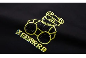 Macro view of yellow bear embroidery with black sequins and XFPARRE lettering on sweatshirt