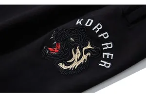 Detailed close-up of intricate wolf head embroidery and white branding on black joggers