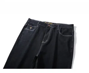 Close-up of dark denim pants with white contrast stitching and gold embroidery details