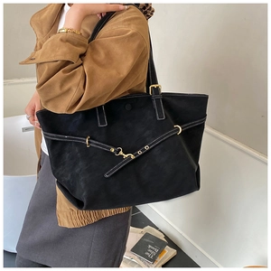 Detail of black tote bag with white contrast stitching and gold buckle worn by model