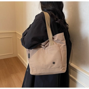 Detail of light brown canvas tote bag with front pocket and durable webbing handle