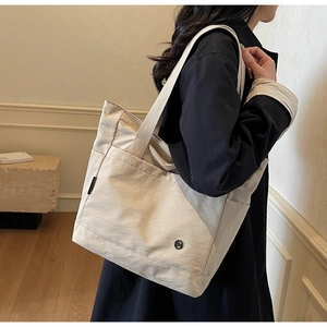 Detail view of a large beige canvas tote bag showing the side pocket and shoulder strap