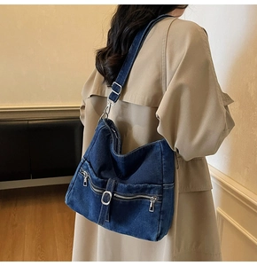 Detail of blue denim tote bag with metal zippers and adjustable silver buckle strap