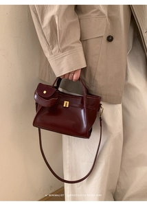 Close-up of deep burgundy glossy leather handbag featuring golden lock and mini charm