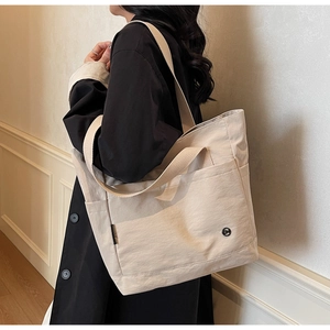Detail of off-white canvas tote bag featuring double straps and outer pocket for daily use