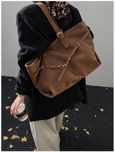 Detail of dark brown suede tote bag with cross straps and gold metal buckle hardware