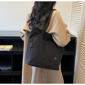 Detail of minimalist black canvas tote bag with brand label worn with a beige trench coat