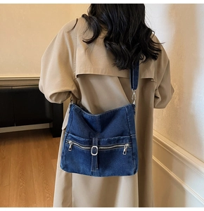Rear view of a model wearing a dark blue washed denim crossbody bag with dual zip pockets
