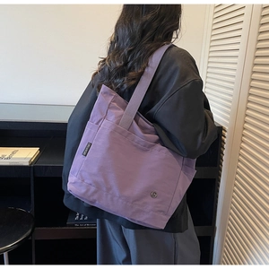 Detailed view of a purple canvas tote bag with side brand label and metal logo detail
