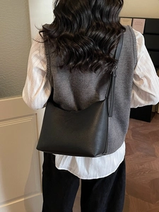 Minimalist black pebble leather hobo bag with adjustable strap worn by a model