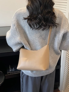 Minimalist beige pebble leather crossbody bucket bag shown on a model in a cozy setting