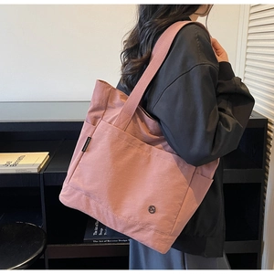 Detail view of large mauve canvas tote bag featuring a brand label and round metal logo