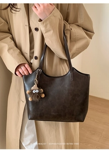 Detail of a dark brown vintage tote bag with a plush charm and glossy leather texture