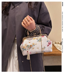 Detailed close-up of vintage floral embroidery, metal clasp, and white tassel on a handbag