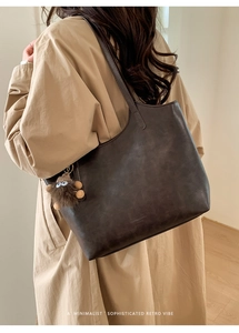 Detail of dark brown leather tote bag with plush charm on a beige trench coat