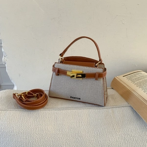 Detailed shot of canvas trapezoid handbag with brown leather trim and gold metal twist lock