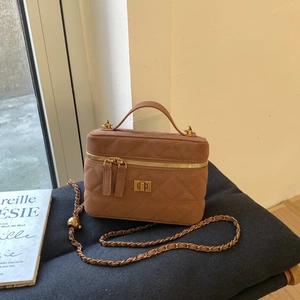 Close-up of brown quilted leather vanity bag with gold chain and metal ball adjuster