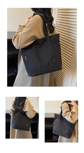 Detail of a large black nylon tote bag featuring front pocket and circular metal logo detail