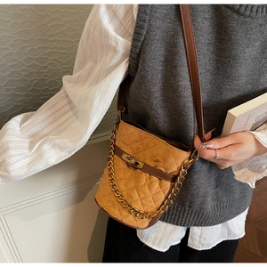 Detail of quilted camel suede bucket bag featuring a gold twist lock and metal chain strap