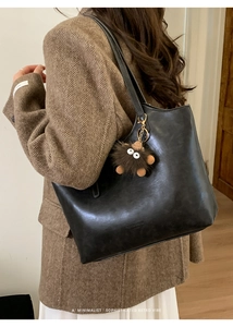 Detail of minimalist black faux leather tote bag with brown plush monster charm and retro vibe