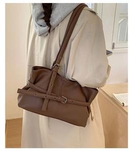 Detail of dark brown litchi pattern tote bag with metal buckles on trench coat