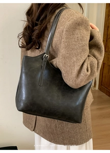 Close-up of a dark grey retro tote bag with matte texture on a model in a tweed blazer