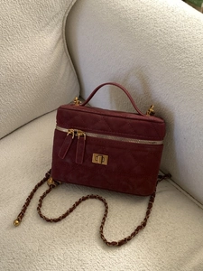 Burgundy quilted crossbody box bag with gold twist lock and chain strap on sofa