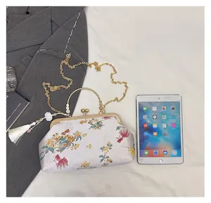 Detail of white embroidery handbag with floral patterns, metal handle and tassel charm