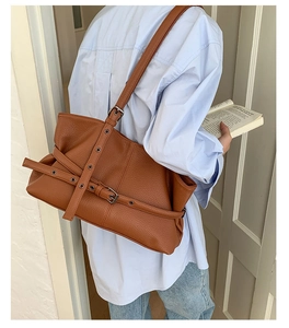 Detail view of brown pebbled leather shoulder bag with vintage metal grommet straps