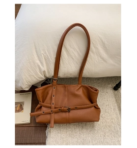 Detail of caramel leather tote bag with pebble texture and metallic buckle accents