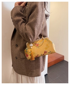 Detail of yellow shell bag with floral patterns, gold chain, and traditional tassel